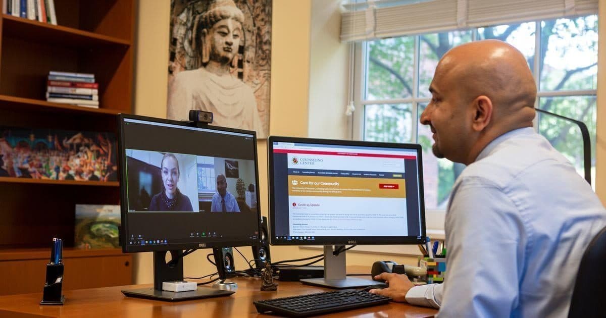 Person sitting at a desk is looking at a monitor with a student on the screen, engaged in a video conference counseling session