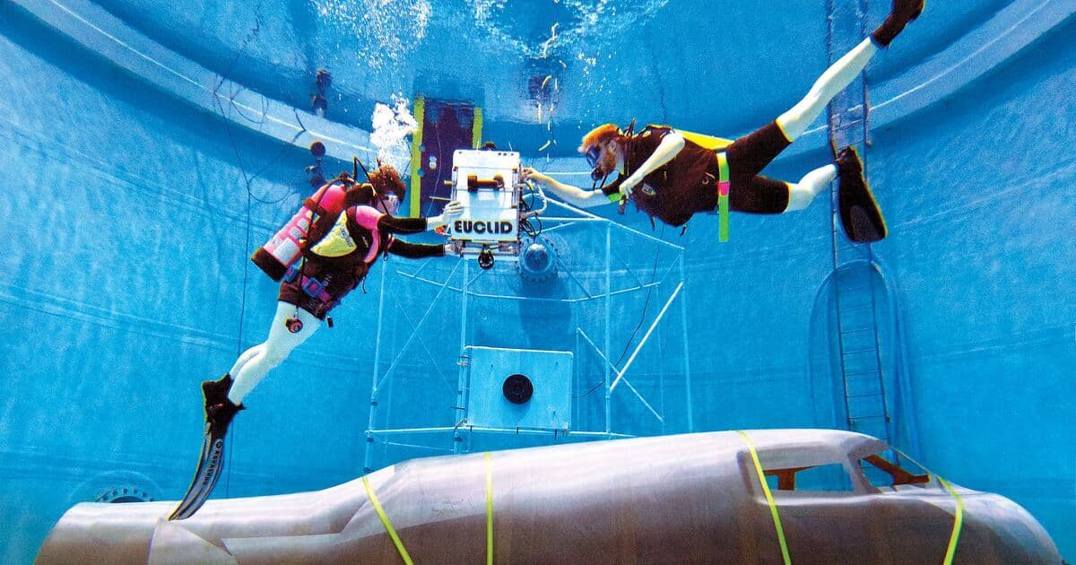 Students scuba diving with a spacecraft fuselage and Euclid, a free-flying underwater robot, in the Neutral Buoyancy tank